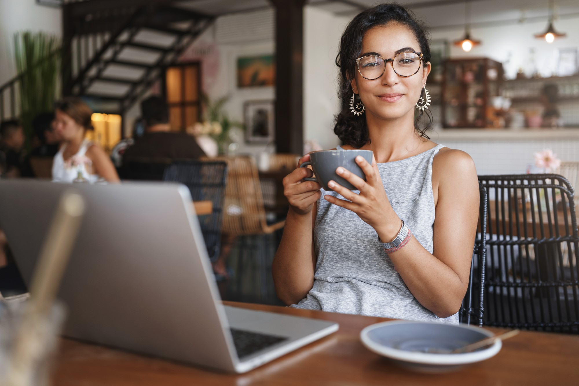 Empreendedora MEI sentada em frente a um notebook sobre a mesa e tomando café